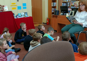 Widok na siedzące dzieci, które wsłuchują się w utwór literacki, czytany przez Panią z biblioteki.