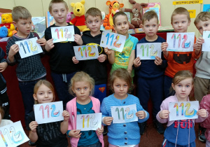 Widok na pozujące dzieci, które w rękach prezentują swoje obrazki z numerem 112.