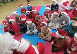 Dzieci siedzą na macie uważnie słuchając Świętego Mikołaja.