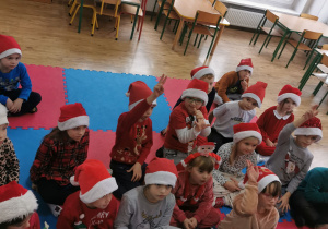Dzieci siedzą na macie uważnie słuchając Świętego Mikołaja.