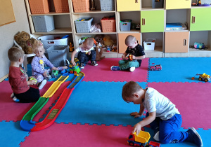 Widok na salę przedszkolną i dzieci, które się wspólnie bawią.