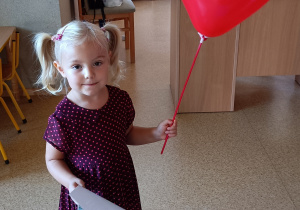 Dziewczynka pozuje do zdjęcia trzymając w dłoniach balon oraz dyplom urodzinowy.