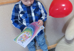 Chłopiec pozuje do zdjęcia trzymając w dłoniach balon oraz dyplom urodzinowy.