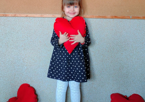 Dziewczynka pozuje do zdjęcia trzymając w dłoniach poduszkę w kształcie serca.