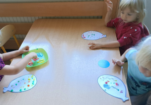Dzieci siedzą przy stoliku. Stemplują palcami kropki na kartonie w kształcie balonika.