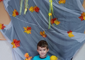 Dziecko pozuje do zdjęcia. W tle znajduje się dekoracja jesienna.