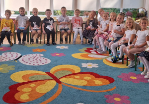 Widok na siedzące dzieci, które trzymają na kolanach drobne upominki z okazji Dnia Przedszkolaka