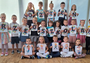 Dzieci pozują do zdjęcia grupowego, trzymając w rękach poszczególne litery tworzące napis Dzień Przedszkolaka.