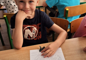Widok na siedzącego chłopca, który maluje sowę przy stoliku.
