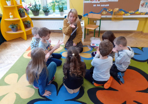 Dzieci wspólnie z logopedą wykonują ćwiczenia oddechowa z słomkami.