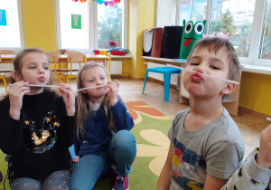 Dzieci wykonują ryjek z ust i próbują utrzymać słomkę.