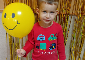 Chłopiec pozuje do zdjęcia, w dłoni trzyma żółty balon, na którym znajduje się uśmiech.