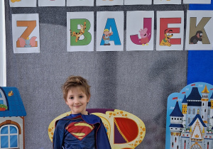 Chłopiec w stroju Superman pozuje do zdjęcia. W tle znajduje się dekoracja z okazji Dnia Postaci z Bajek.