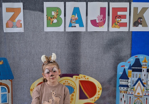Dziewczynka w stroju jelonka Bambi pozuje do zdjęcia. W tle znajduje się dekoracja z okazji Dnia Postaci z Bajek.
