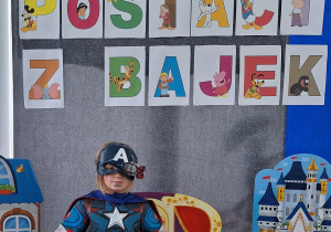 Chłopiec w stroju Avengers-a pozuje do zdjęcia. W tle znajduje się dekoracja z okazji Dnia Postaci z Bajek.