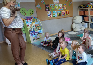 Widok na siedzące dzieci oraz stojącą Panią z biblioteki, która ma na swojej ręce nałożoną pacynkę.