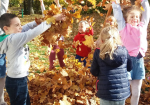 Grupka dzieci bawi się liśćmi podrzucając je do góry.