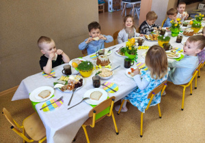 Widok na dzieci siedzące przy pięknie udekorowanym wielkanocnym stole, które wspólnie spożywają przygotowane świąteczne śniadanie.