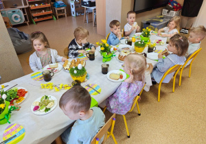Widok na dzieci siedzące przy pięknie udekorowanym wielkanocnym stole, które wspólnie spożywają przygotowane świąteczne śniadanie.