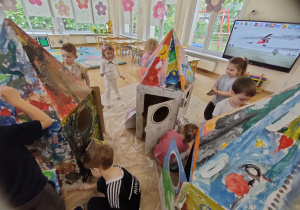 Widok na dzieci malujące tekturową rakietę 3D.
