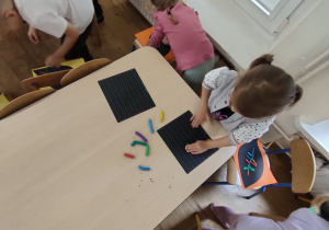 Widok na dzieci, które rozwałkowują plastelinę i przyklejają ją na kartkę z wyciętym liściem.