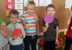 5 dzieci stoi na tle tablicy trzymając w rękach kolorowe kółka.