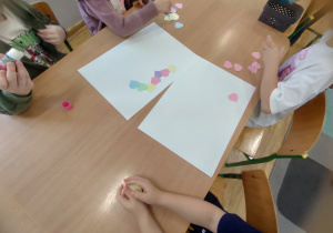 Widok na dzieci, które tworzą kształt serca za pomocą serc papierowych.