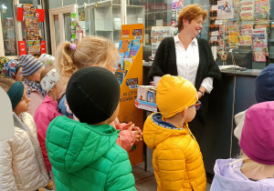 Widok na grupę dzieci, które z uwagą słuchają Pracownika Urzędu Pocztowego w budynku Poczta.