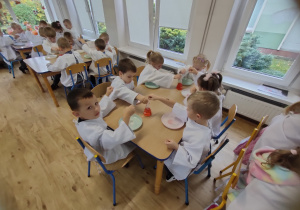 Widok na dzieci siedzące przy stole w stroju chemika i wykonujące indywidualnie eksperyment.