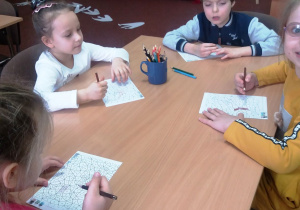 Dzieci siedzą przy stoliku i kolorują rysunek dinozaura.