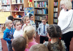 Dzieci znajdują się w bibliotece pedagogicznej. Przed nimi stoi pani, która opowiada im o barwach jesieni.
