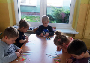 Dzieci siedzą przy stoliku, przed nimi leżą paski matematyczne, które szeregują według wielkości.