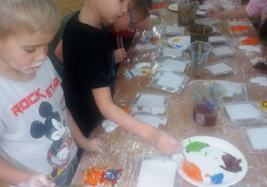 Widok na stół, przy którym dzieci malują swoje figurki z gipsu.