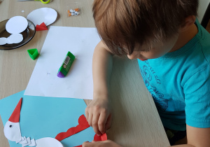Chłopiec wykonuje pracę plastyczną przedstawiającą bociana na niebieskim tle.