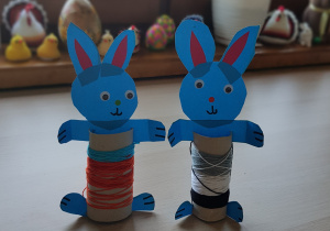 Praca plastyczno- techniczna przedstawiająca dwa uśmiechnięte zajączki wykonane z niebieskiego papieru kolorowego i rolek po papierze toaletowym.