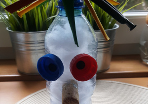 Ekoludek Antosia. Wykonany z butelki plastikowej, włosy ma z gazet, oczy z nakrętek plastikowych, nos z korka, usta zaznaczone czerwoną plasteliną.