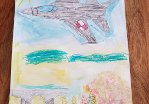 Praca plastyczna Juliusza. Chłopiec namalował rynek naszego miasta z pomnikiem „Walczącym o niepodległość Ojczyzny”, drzewami i niebem po, którym szybuje wojskowy samolot F-16.