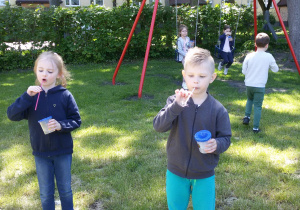 Dzieci w ogrodzie przedszkolnym puszczają bańki mydlane.