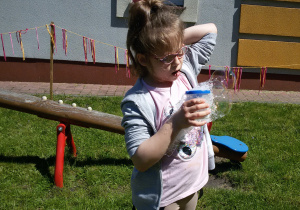 Oliwia puszcza bańki mydlane w ogrodzie przedszkolnym.