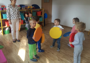 Grupa dzieci bawi się z nauczycielką. Każde dziecko trzyma w ręku kolorowy krążek.