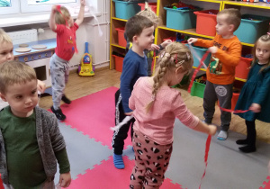 Grupa dzieci tańczy z biało-czerwonymi paskami bibuły.