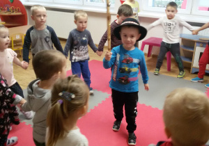 Dzieci trzymają się za ręce tworząc koło, w środku stoi Olek w góralskim kapeluszu i ciupagą.