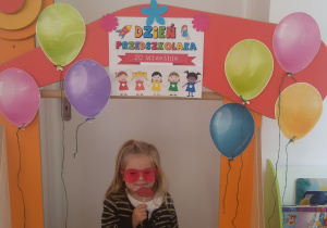 Marysia pozuje do zdjęcia na tle ozdobionej balonami ramki z napisem Dzień Przedszkolaka 2020.