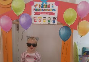 Jagoda pozuje do zdjęcia na tle ozdobionej balonami ramki z napisem Dzień Przedszkolaka 2020.