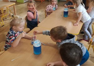 Dzieci siedzą przy stolikach i eksperymentują z niebieskim barwnikiem.