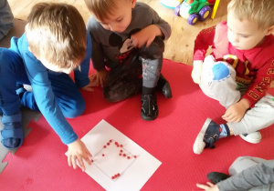 Dzieci układają z czerwonych koralików kwadrat.