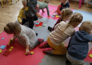 Dzieci siedzą na dywanie i układają obrazki z figur.