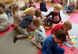 Dzieci siedzą na dywanie i układają obrazki z figur.