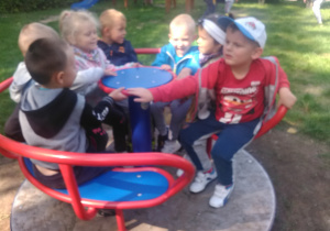 Na placu przedszkolnym grupka dzieci bawi się na karuzeli.