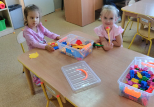 2 dziewczynki siedzą przy stoliku i budują z klocków.